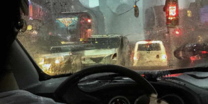 AI Image - Realistic image of a man driving a car in the streets of New York looking through the window and seeing the rain outside in a heavy traffic.